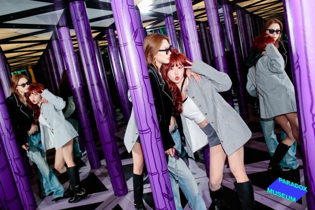 Two women posing in a mirrored room with purple columns, creating a kaleidoscopic effect, at the Paradox Museum.