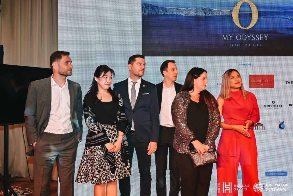 A group of professionals posing together on stage at an event with a digital backdrop featuring the My Odyssey logo and sponsor names.